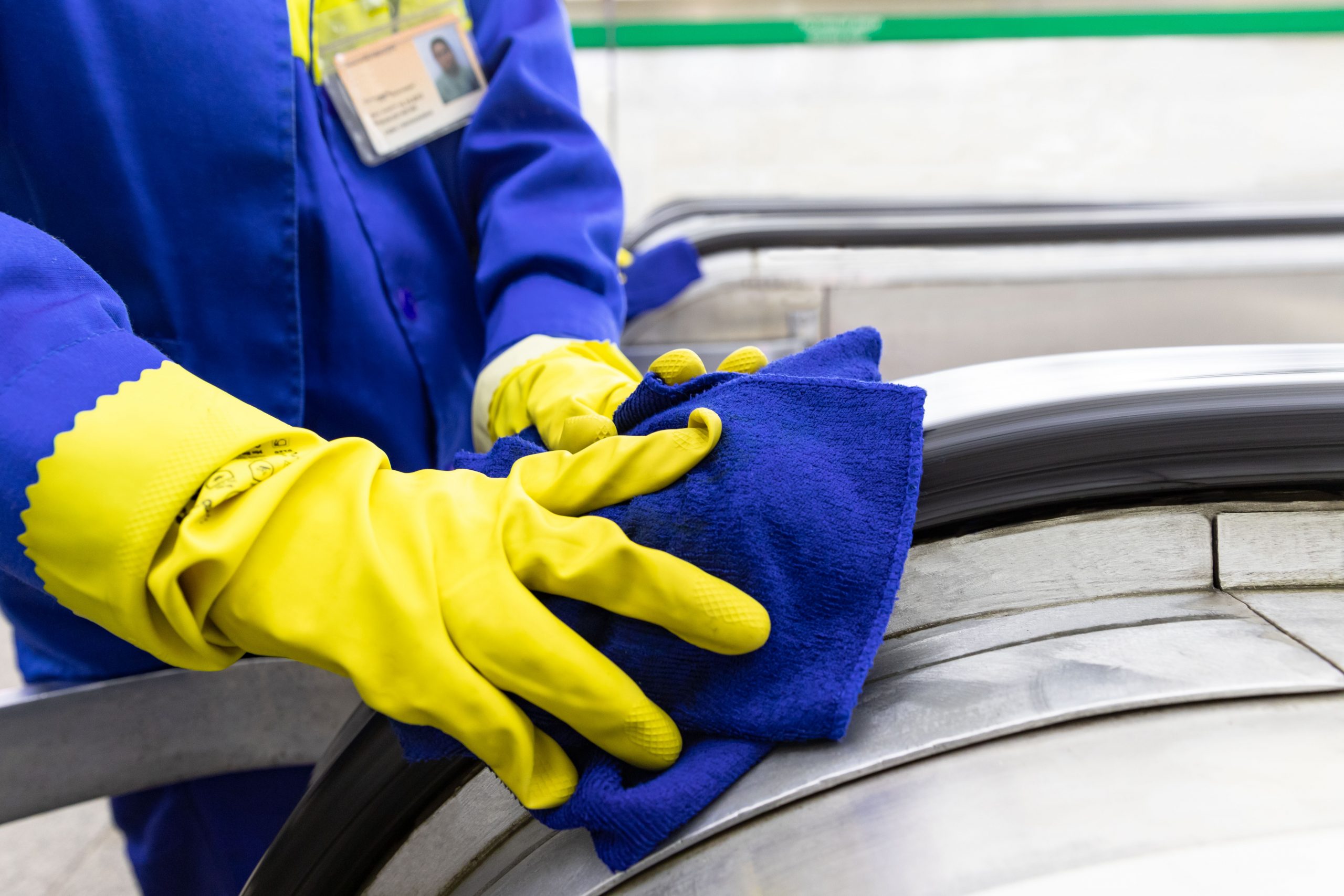 close up of employee with yellow gloves using a blue cloth cleaning escalator handrail